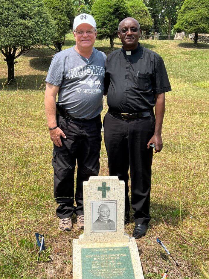 Priest and visitor standing by cemetery headstone