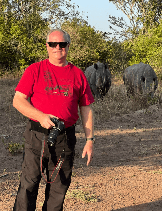 Man with camera posing near two rhinos